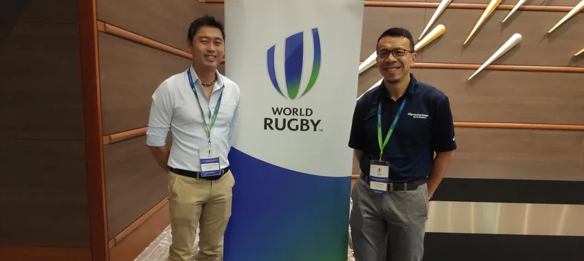 Dr Lai and a colleague beside a World Rugby banner at an event in 2019